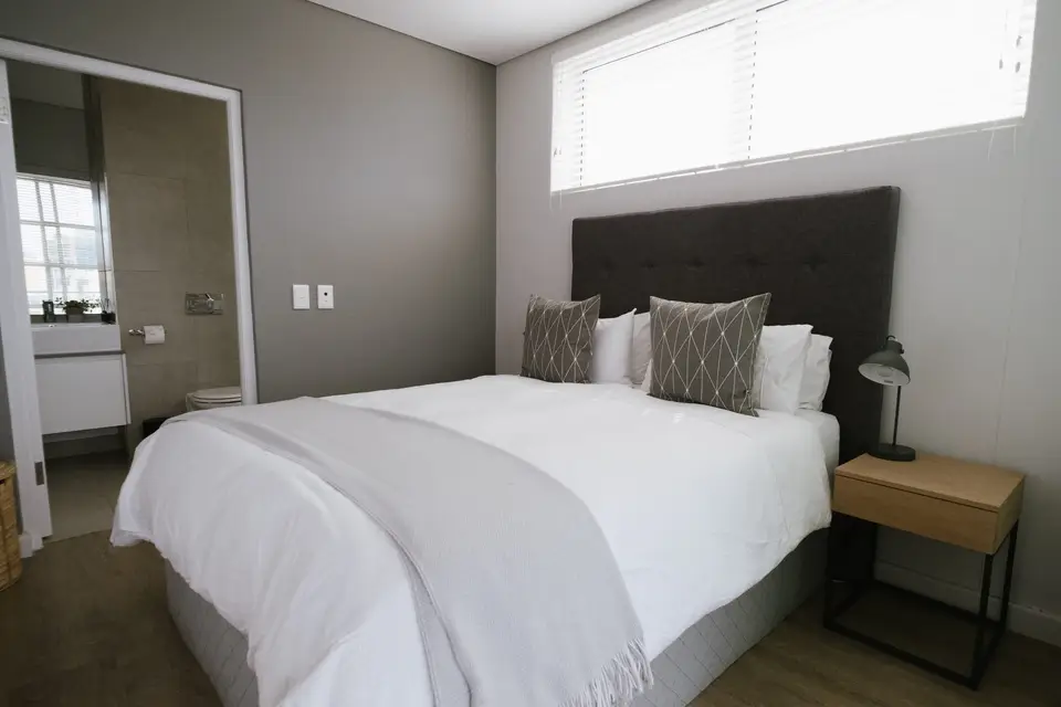A bedroom made up with fresh white linen, a bathroom beyond