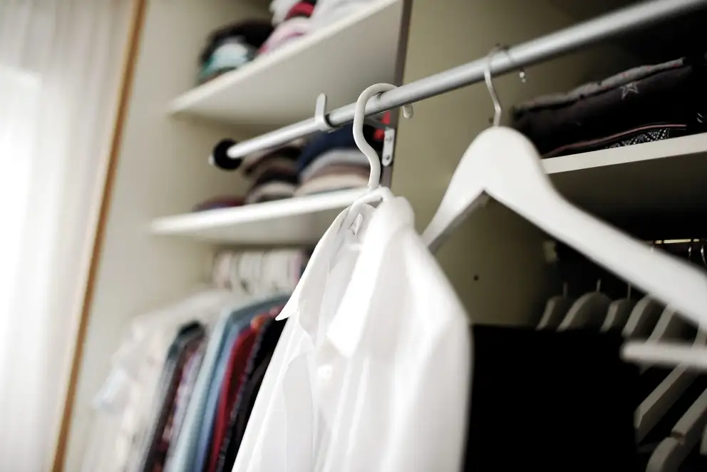 White shirts on hangers in a wardrobe, folded clothes on the shelves