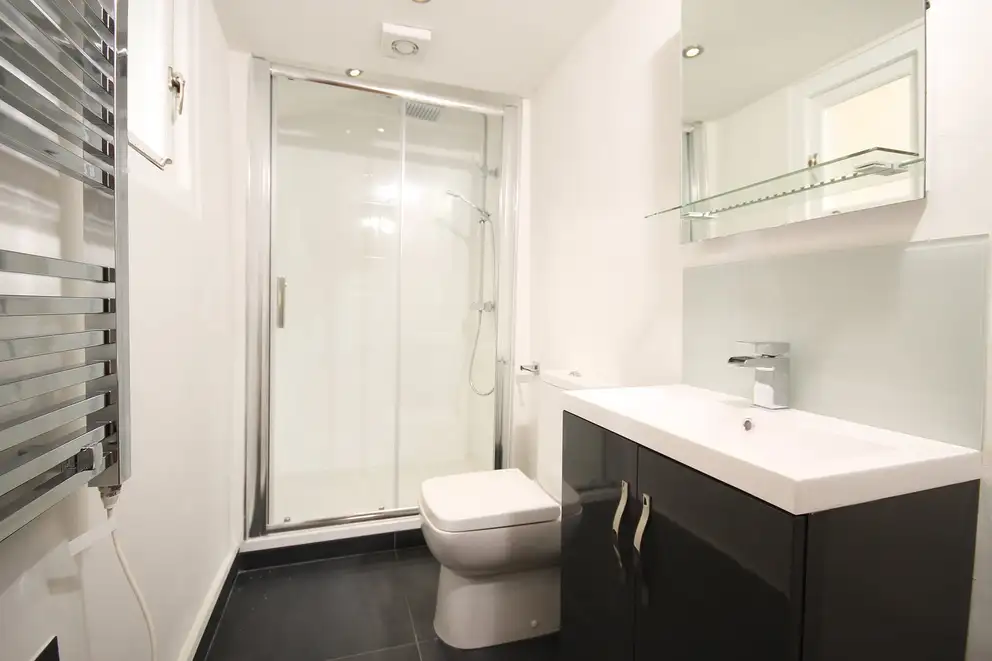 A white bathroom with a glass shower and a dark vanity