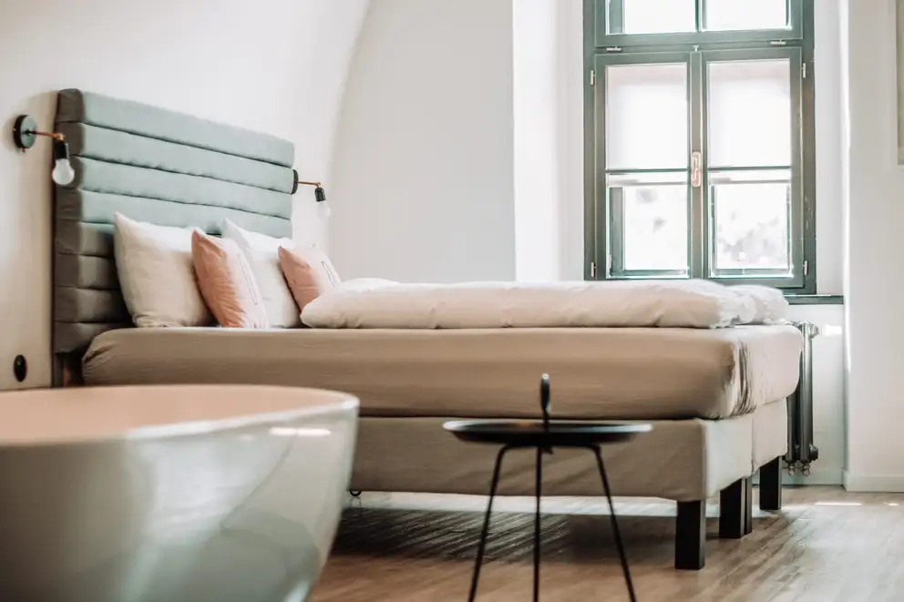 A made bed with an upholstered headboard beside a tall window