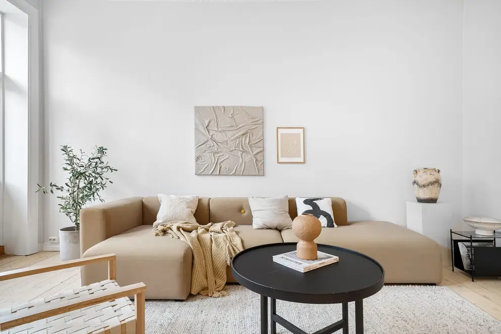 A living room with a beige sofa, a round coffee table and a plant by the window