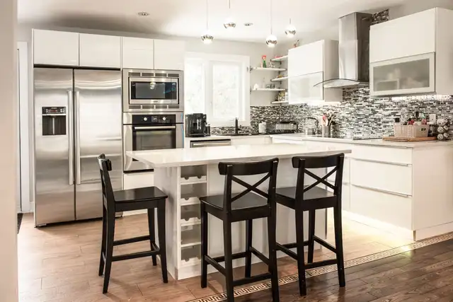 A white kitchen with an island, three bar stools and steel appliances