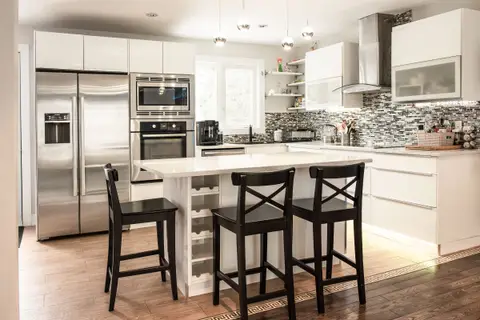 A white kitchen with an island, three bar stools and steel appliances
