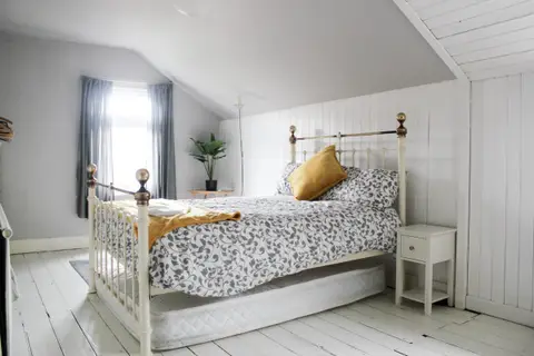 An attic bedroom with a brass bed, white wood walls and a window