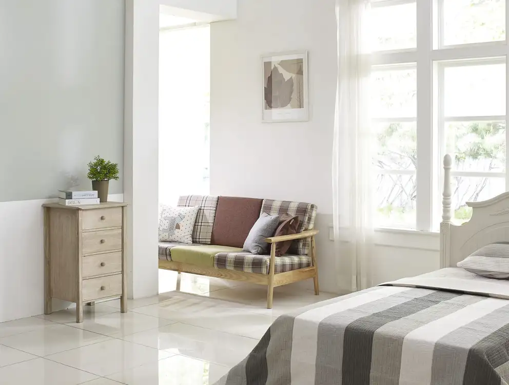 A bedroom with a made bed, an armchair and a bright window