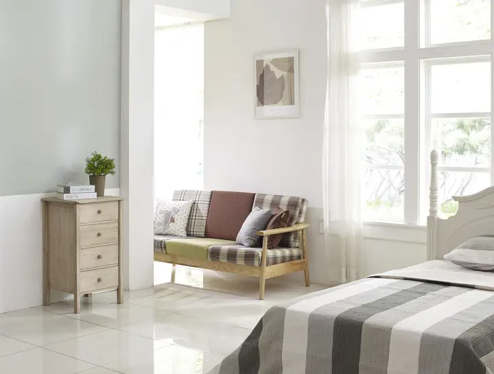 A bedroom with a made bed, an armchair and a bright window