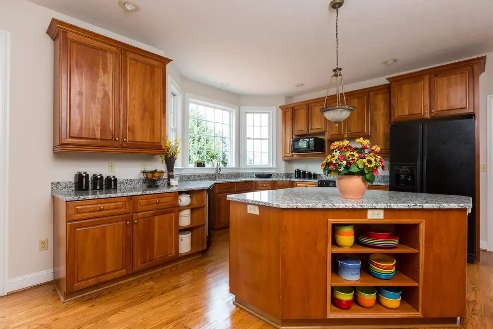 A kitchen with wood cabinets, a granite island and a bay window