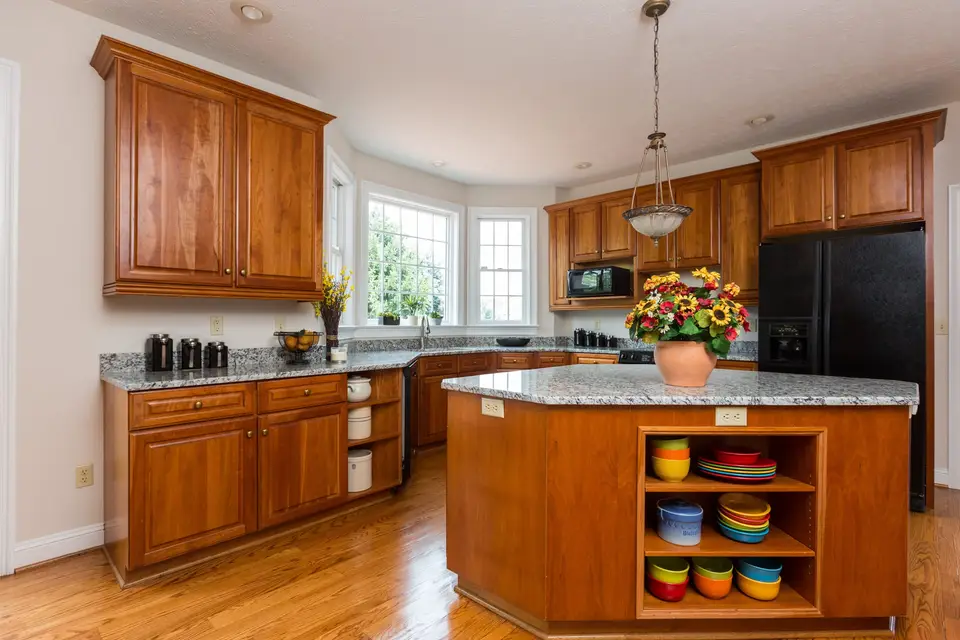 A kitchen with wood cabinets, a granite island and a bay window