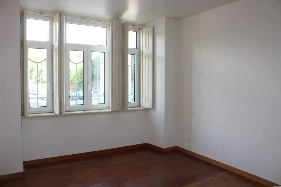An empty room with a bare wood floor and an open window