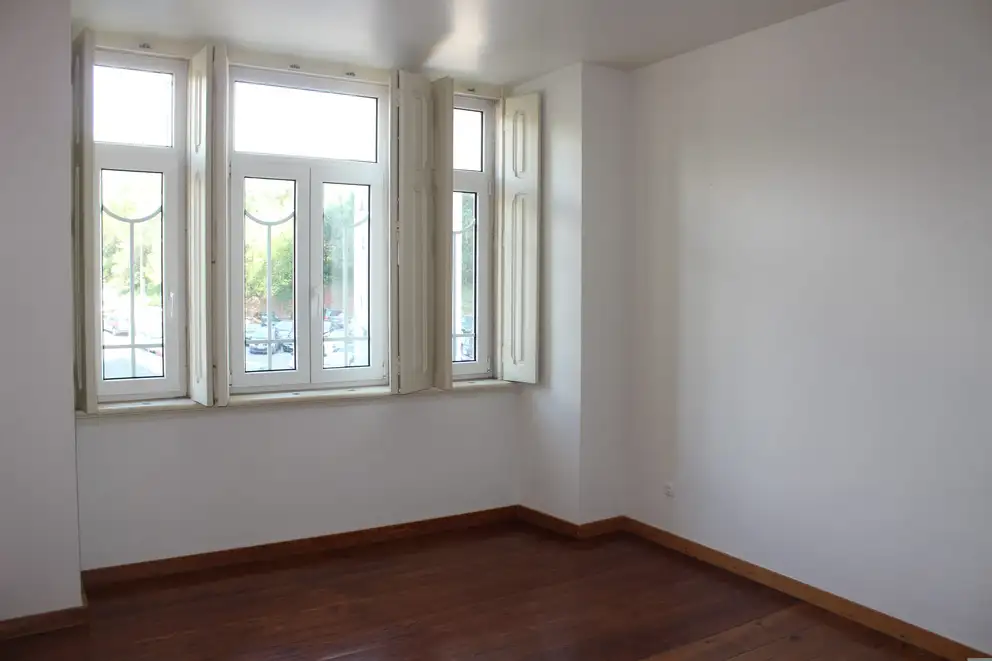 An empty room with a bare wood floor and an open window